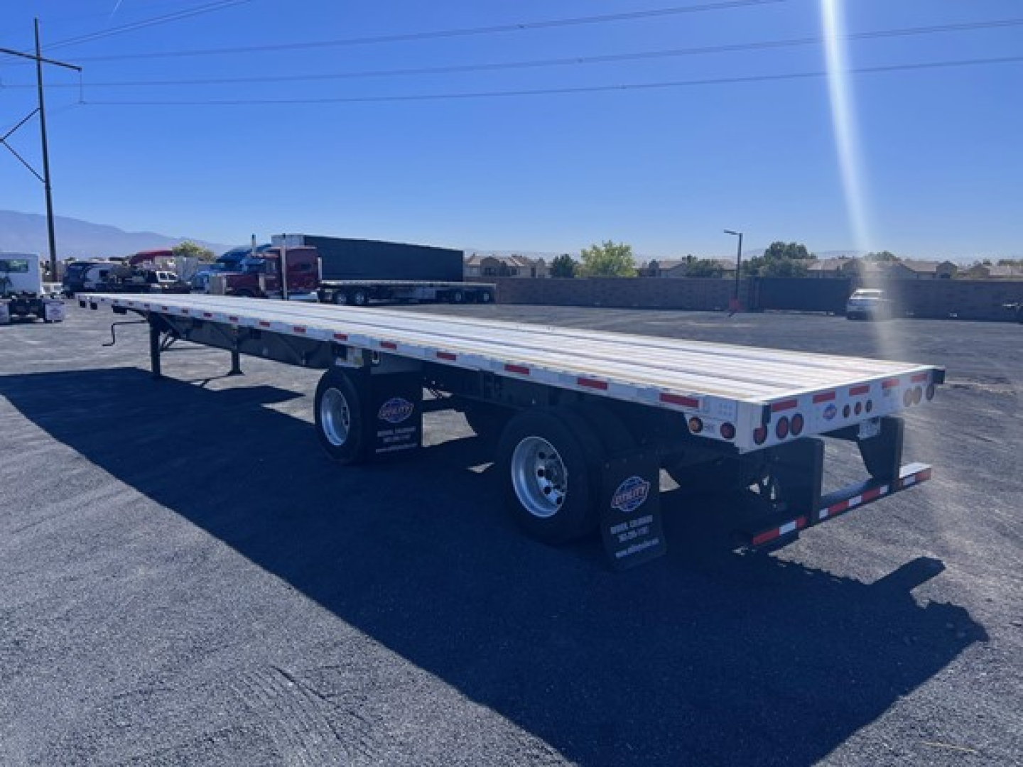Flatbed trailer showing dual rear axles and long aluminum deck with reflective tape and rear lights.