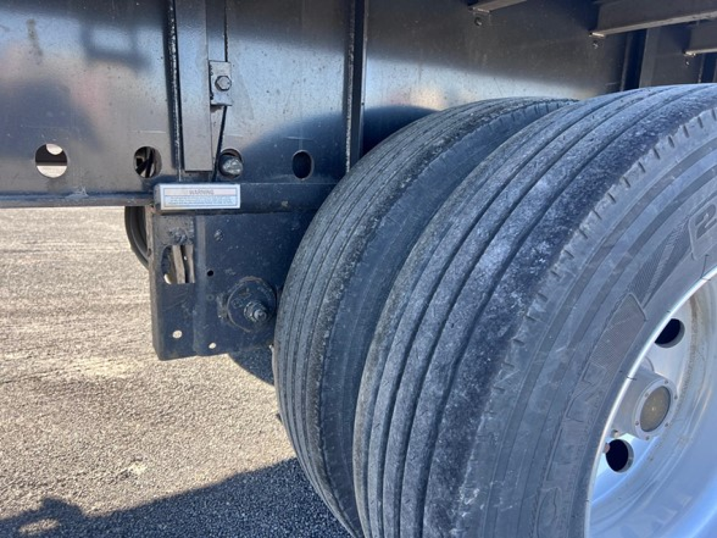 Utility trailer wheel and suspension area showing dual tires and frame with label plate. 2024 Utility 4000AE trailer context text not visible.