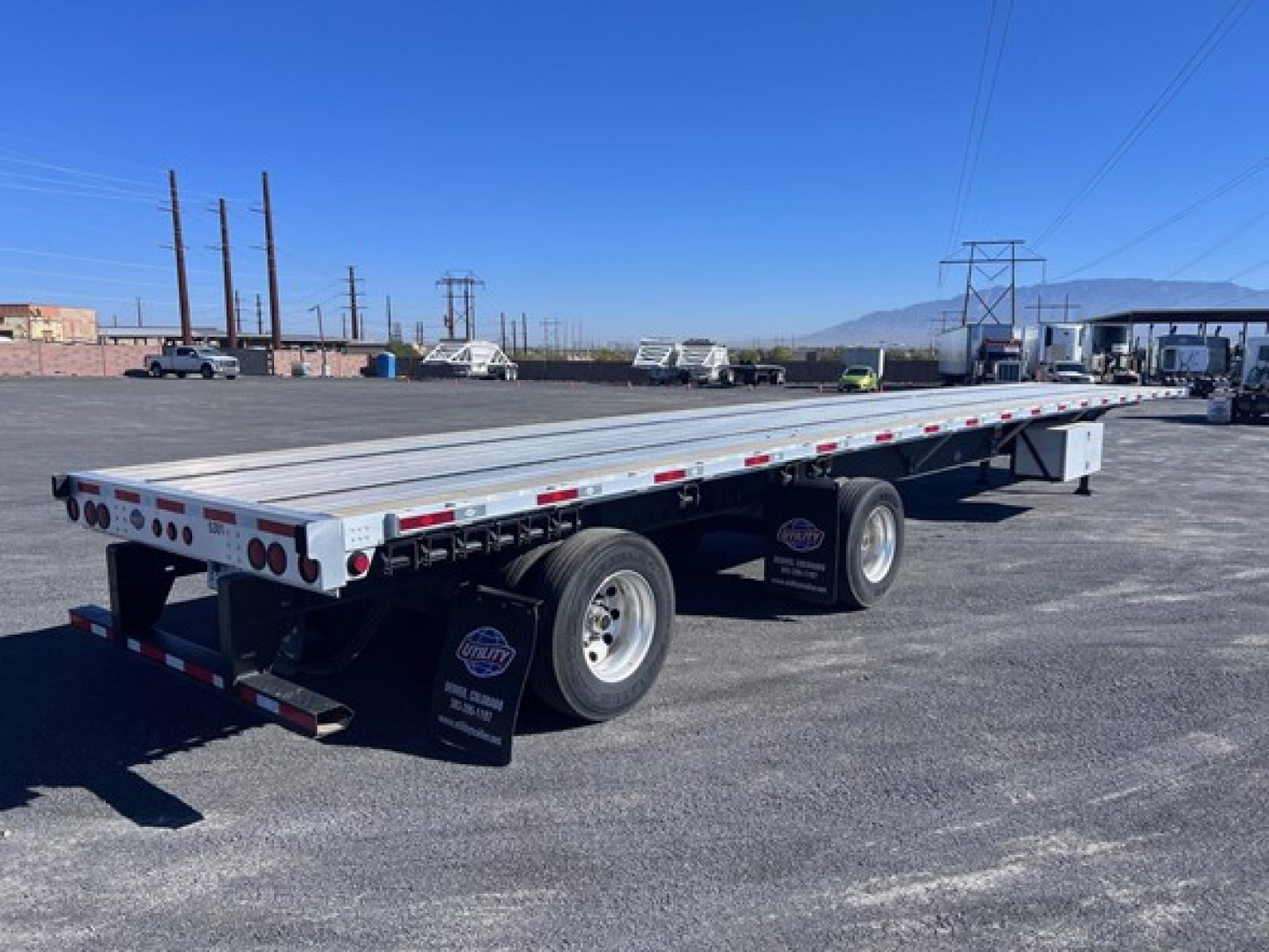 Flatbed trailer showing long aluminum deck with dual rear axles and black mud flaps, Utility logo visible, outdoor lot.