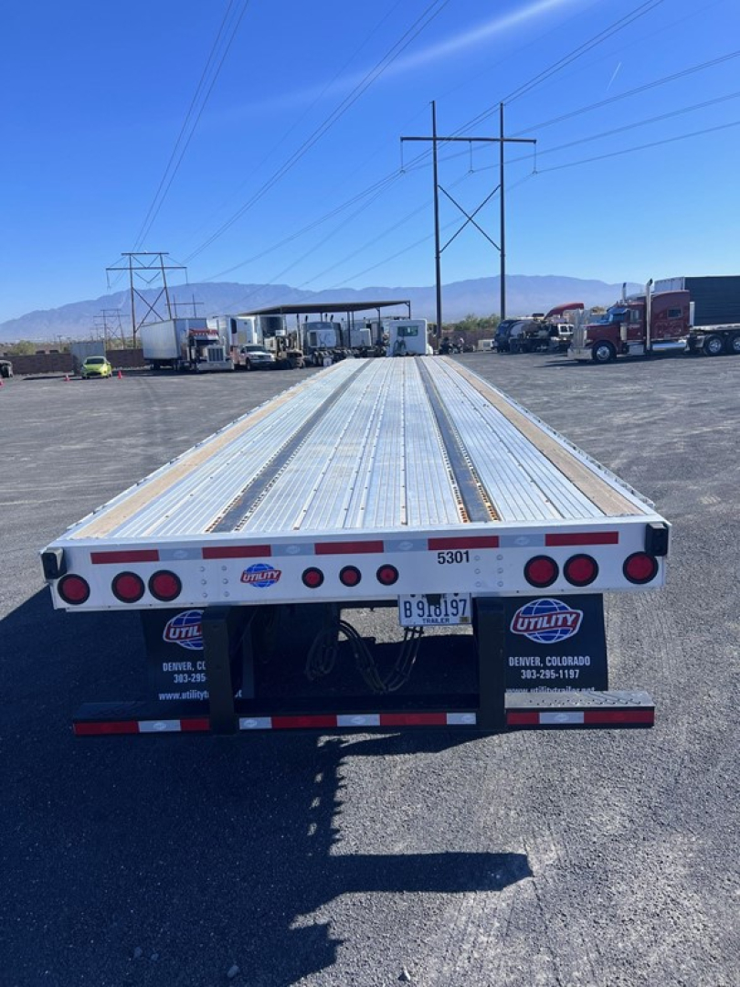 Flatbed trailer in-service showing long aluminum deck, back lights, and bumper with Utility logo.