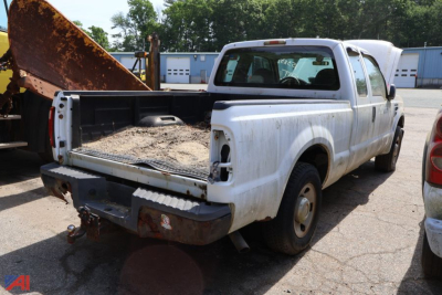 Ford F-250 Super Duty pickup bed area showing rear with cargo bed and tailgate, white with dirt and a rusty dumpster nearby.
