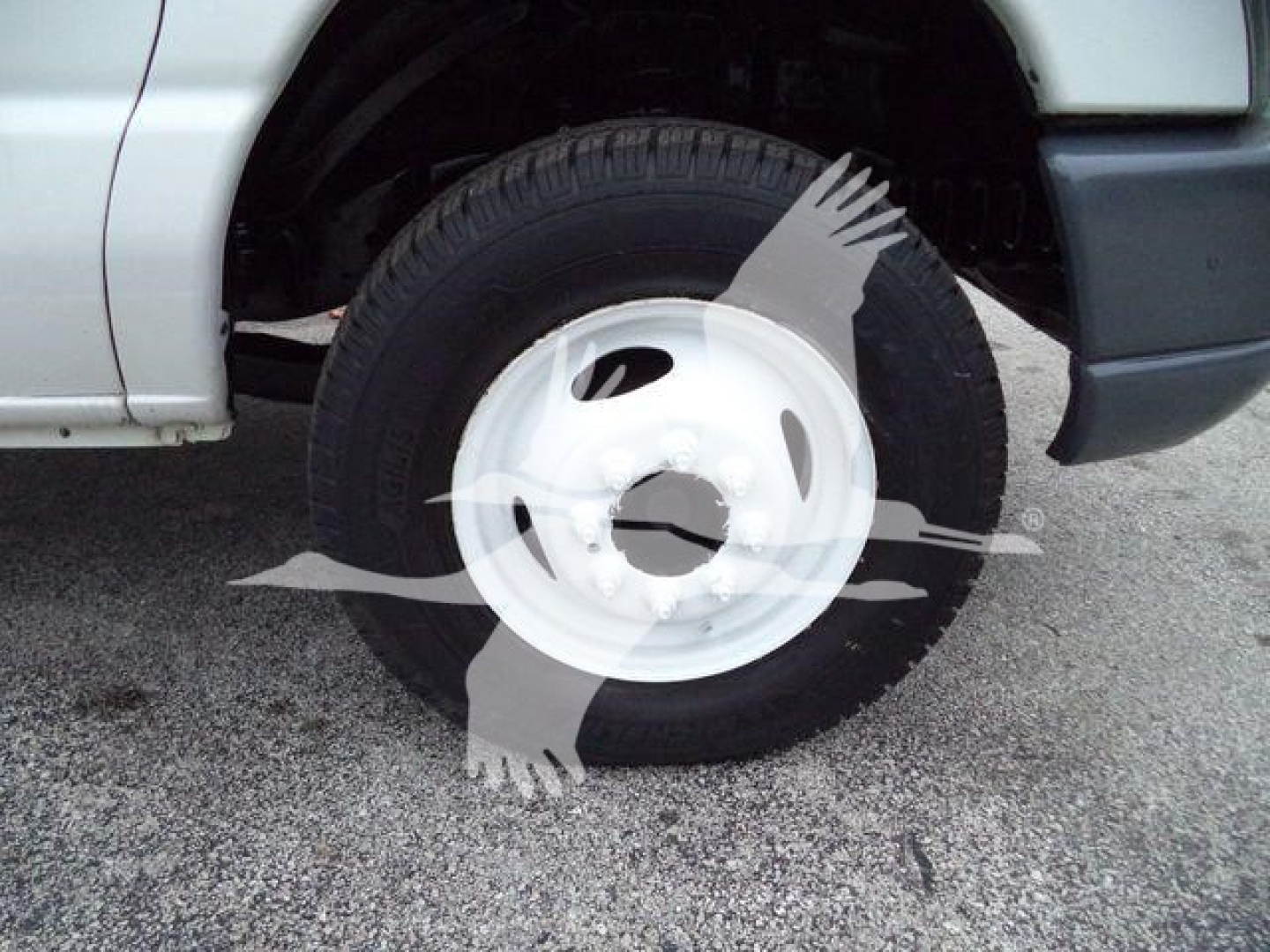 Ford E450 wheel area showing front tire and white steel wheel, partial front fender and splash guard.