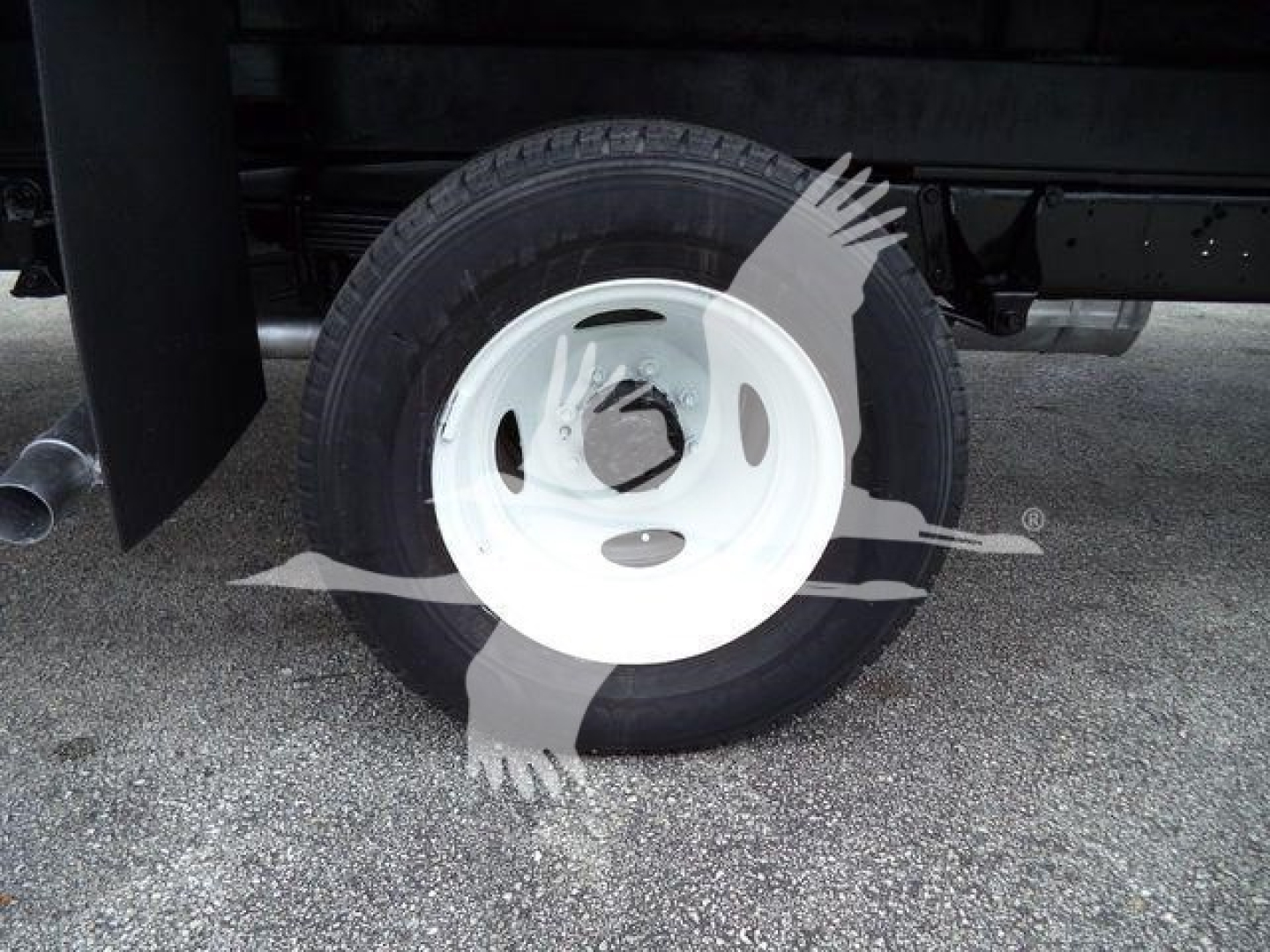 Ford E450 wheel and tire visible under a box truck body, white steel rim, black tire, with faint dark area around.