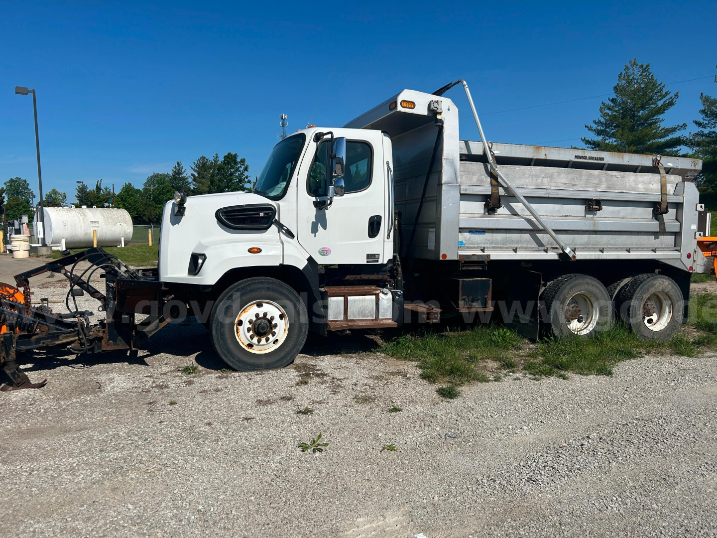 Truck side view showing a white Freightliner 108SD dump truck with plow attachment and gray dump bed.