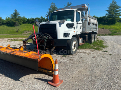 Dump truck with large snow plow attachment in front, white Freightliner 108SD, dual rear axles, plow orange with white and black accents, traffic cone in foreground.