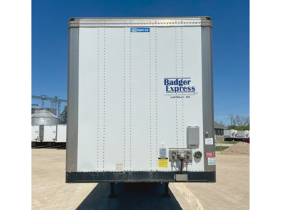 Rear view of a white Badger Express trailer with blue logo, doors closed, wheel chocks visible, stock number plate, and VIN label on rear.