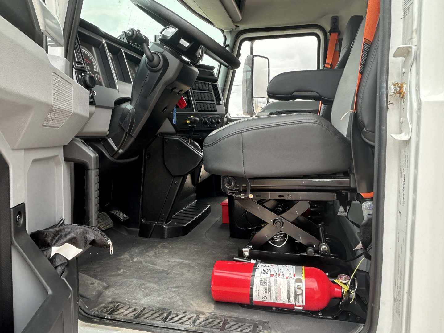 Cab interior of a 2026 Mack MD6 with steering wheel, driver seat, and red fire extinguisher on floor; dashboard and controls visible.