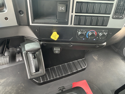 MD6 truck dashboard area showing ignition switch, HVAC controls, yellow hood latch, and footwell with rubber mat.