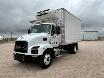2026 Mack MD6 refrigerated truck with front grille, black bumper, white cab, and insulated box; Merrowing refrigeration unit on top front of box; dash of tires in gravel lot.