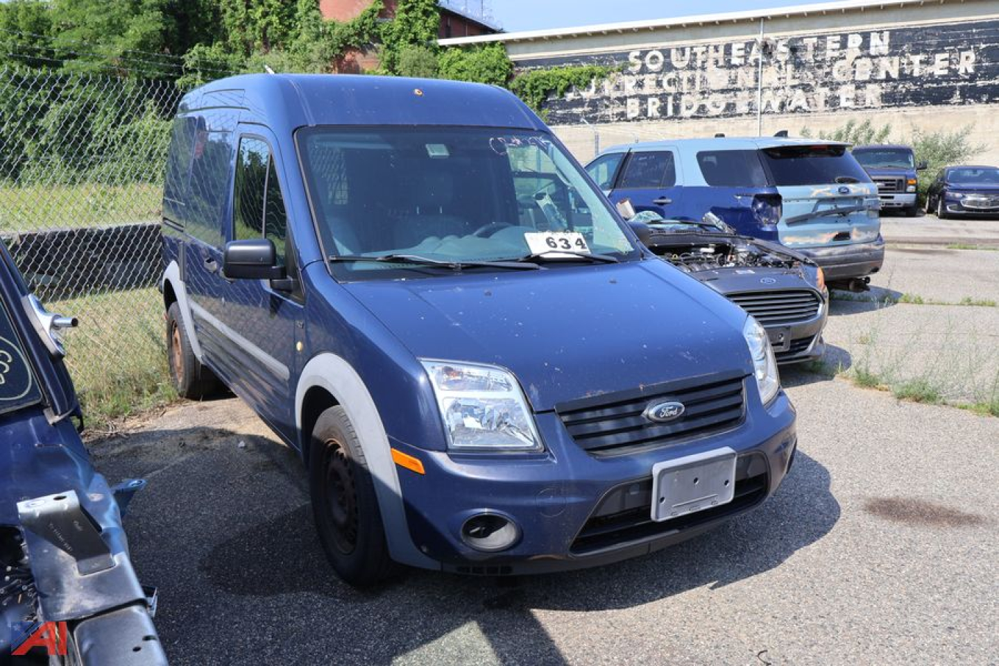Ford Transit Connect cargo van in blue, front-left view with raised hood and windshield, number 63 on windshield, dealership lot in background.