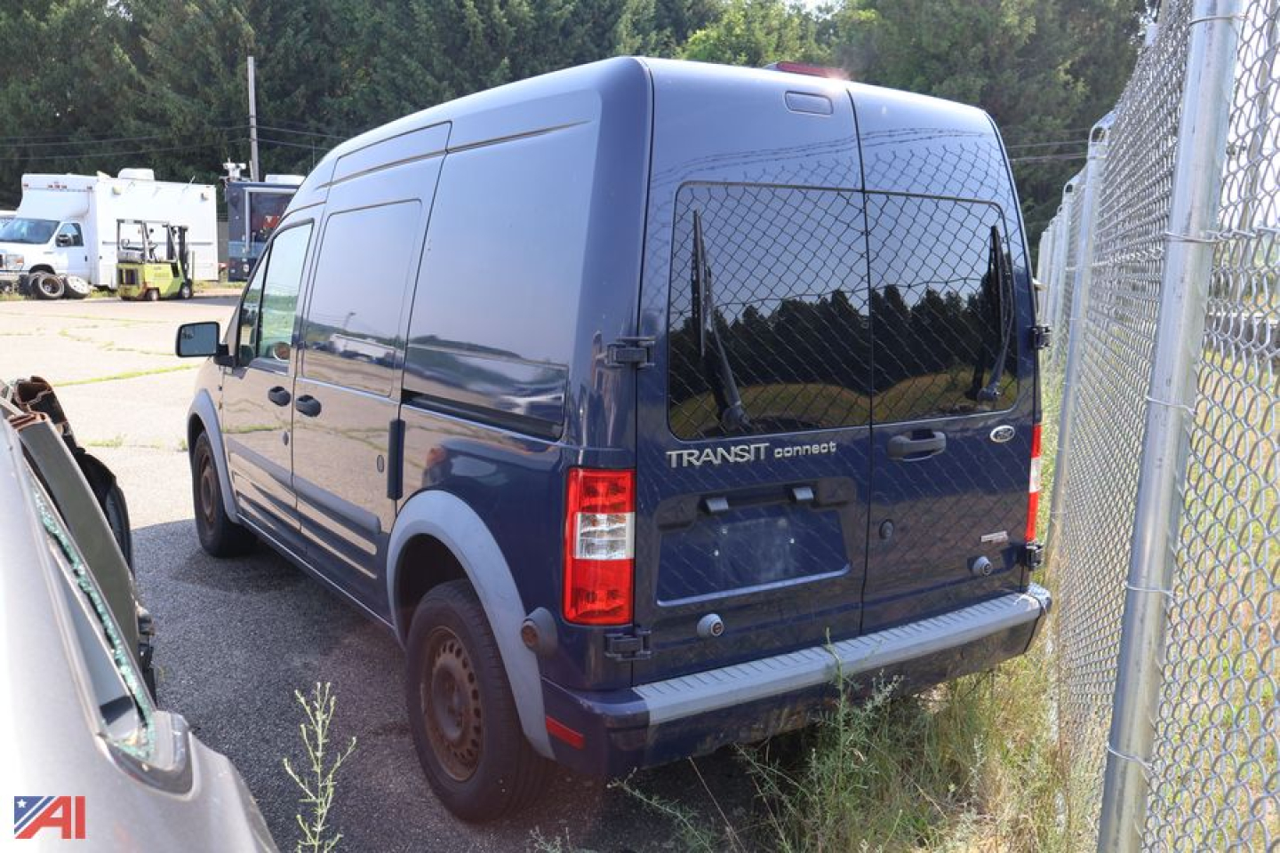 Ford Transit Connect cargo van rear view showing back doors and taillights, blue color, parked near chain-link fence.