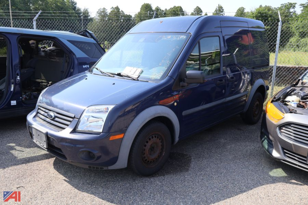 Ford Transit Connect cargo van in blue, front-left view, missing front passenger wheel cover, basic steel wheel, side mirrors, daytime.