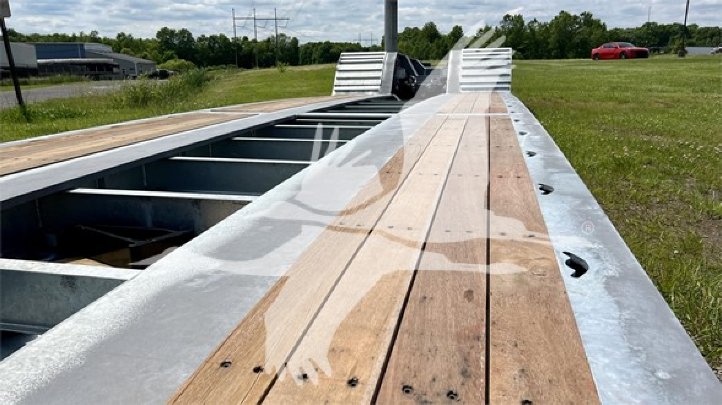 Trailer deck with wooden planks and metal frame, viewed from side, long lowboy trailer hub area exposed.