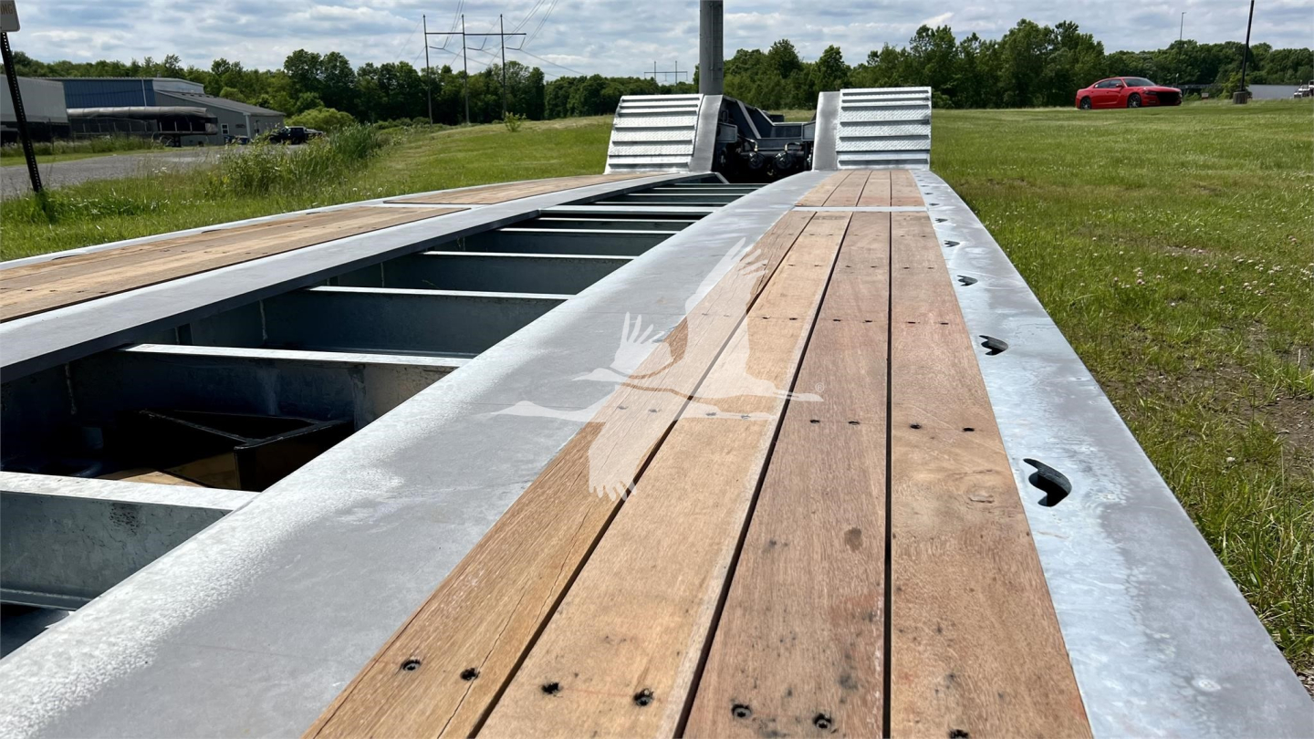 Trailer deck of XL Specialized XL110HDGS showing wooden planks and steel frame with open gaps for wheel wells, outdoor field background.