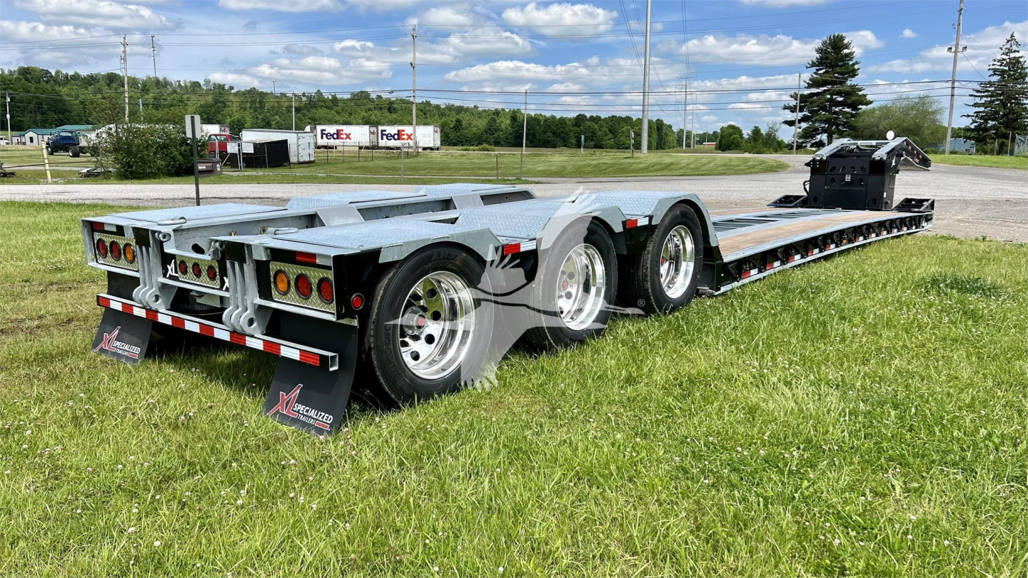 Trailer chassis with multi-axle lowboy trailer showing steel deck, dual rear axles, and rear lights in a grassy lot.