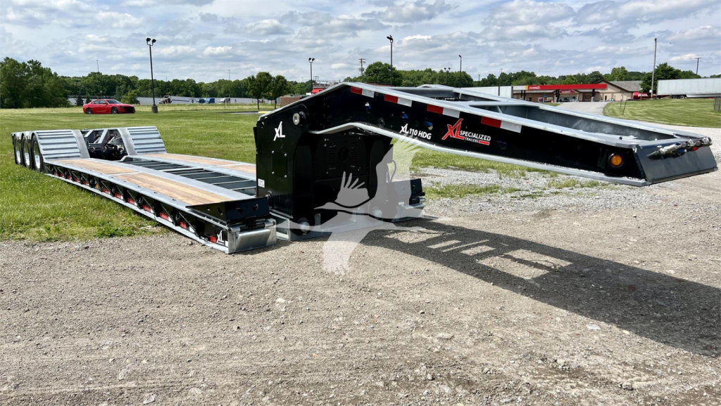 Lowboy trailer with extended flat deck showing XL Specialized XL110HDGS branding and wheel/axle area; clear sky and gravel lot.