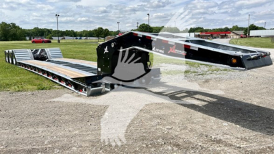 Lowboy trailer in an open lot, black and silver with ramp sections, branding on side, long length with multiple axles, tire wheels visible, oil/industrial equipment surroundings.