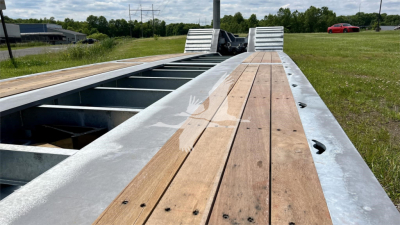 Trailer deck of XL Specialized XL110HDGS showing wooden planks and steel frame with open gaps for wheel wells, outdoor field background.