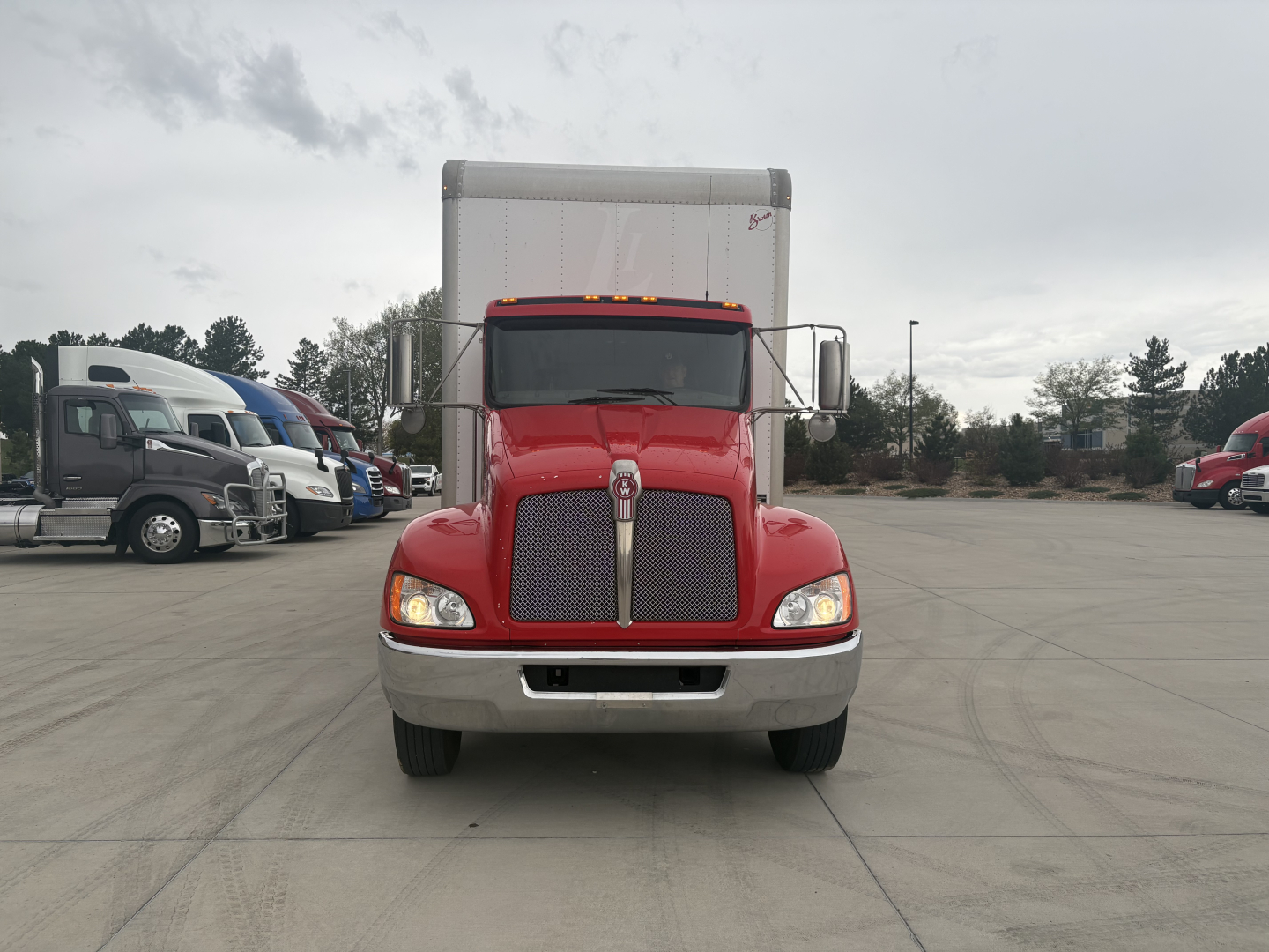 Kenworth T270 front view in red with large silver grille and aluminum cab, box truck with matching bumper and round headlights.