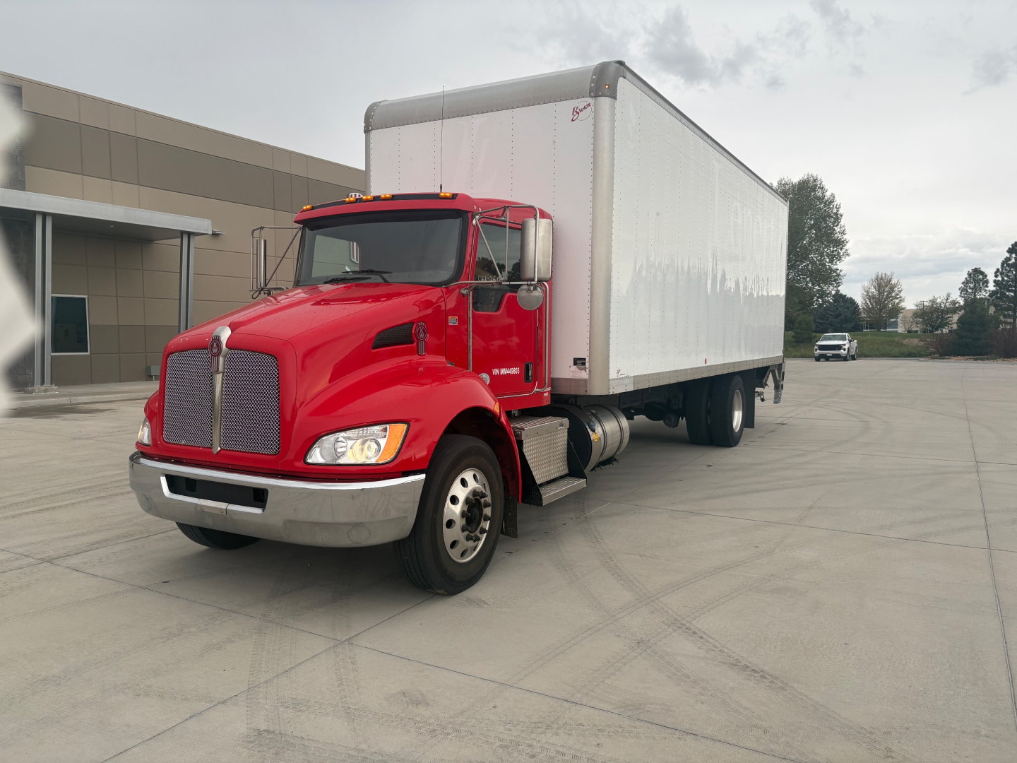 Truck cab and box trailer of a red 2021 Kenworth T270, front-left view, with a white box body and dealership lot backdrop.