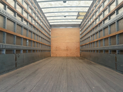 Kenworth box truck cargo area interior showing wood floor and metal side walls with rails, empty cargo space.