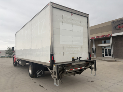 Kenworth box truck rear view showing white cargo area with reflective stripes and rear underride guard; back door panel with blank label area; dual rear wheels.