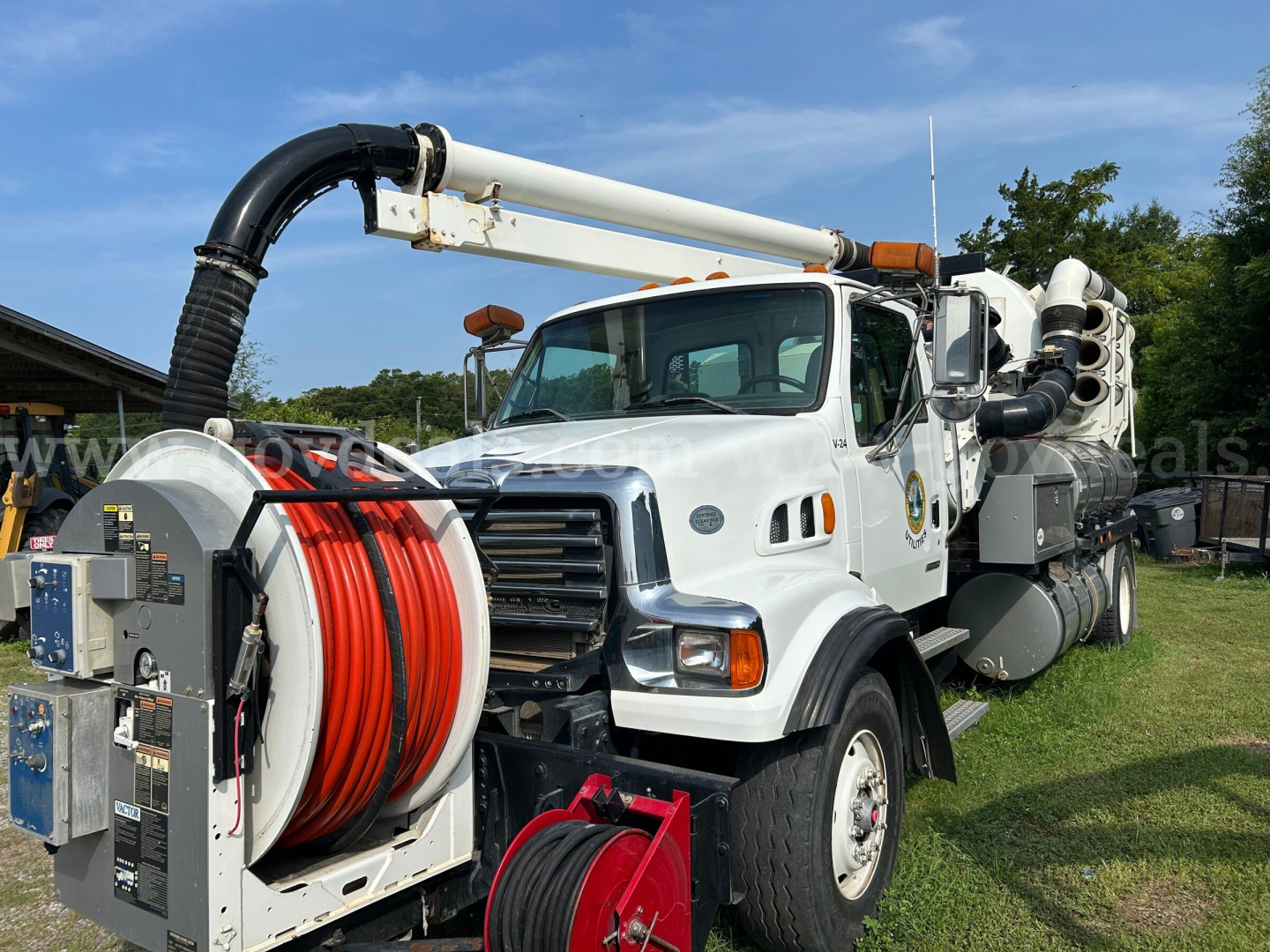 Truck chassis with large vacuum hose reel and hose reels; front grille and cab visible; high pressure vacuum system mounted on back; white truck with black hose, red and white hose reels, and hydraulic arm.