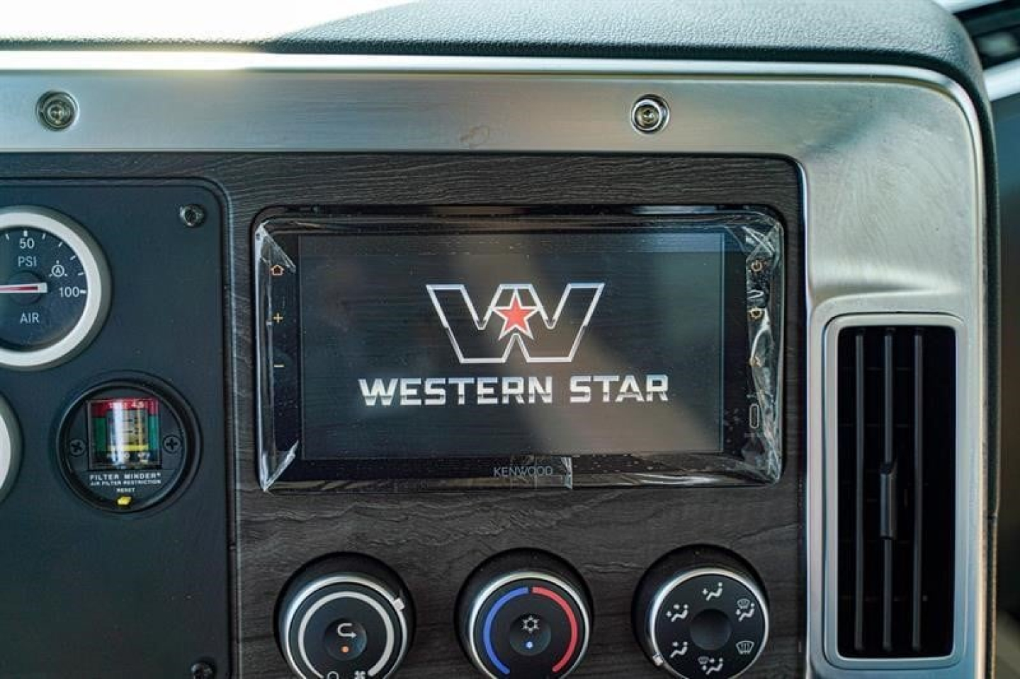 Dashboard display showing Western Star logo on center screen with control knobs and air gauge on left in a roll-off truck cabin