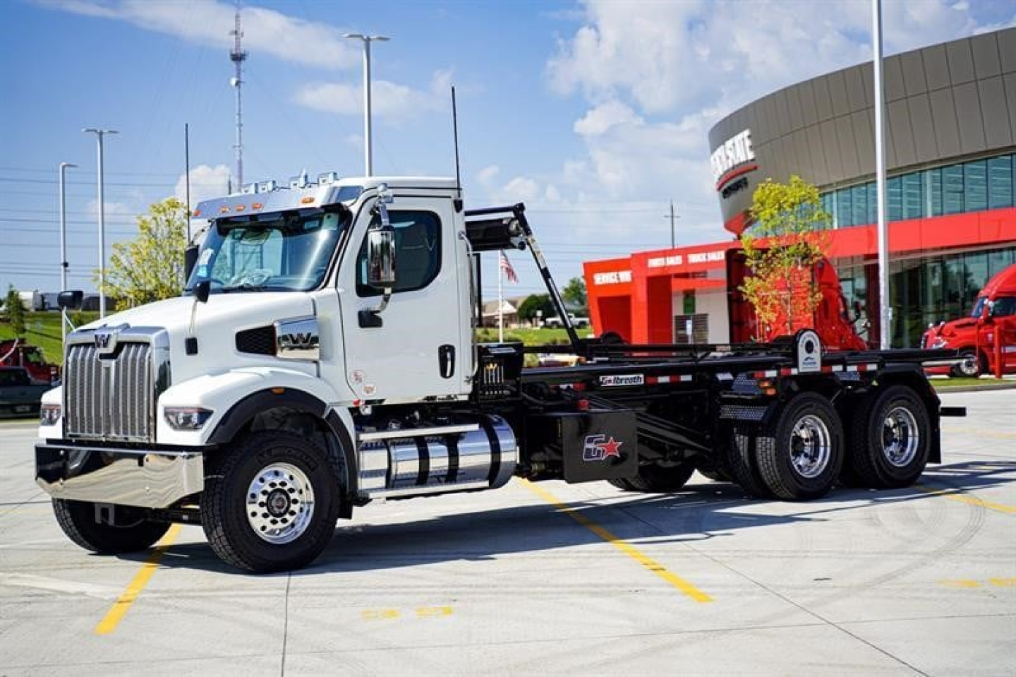 White Western Star 47X roll-off truck in a dealership lot showing chassis and cab details with empty bed frame.