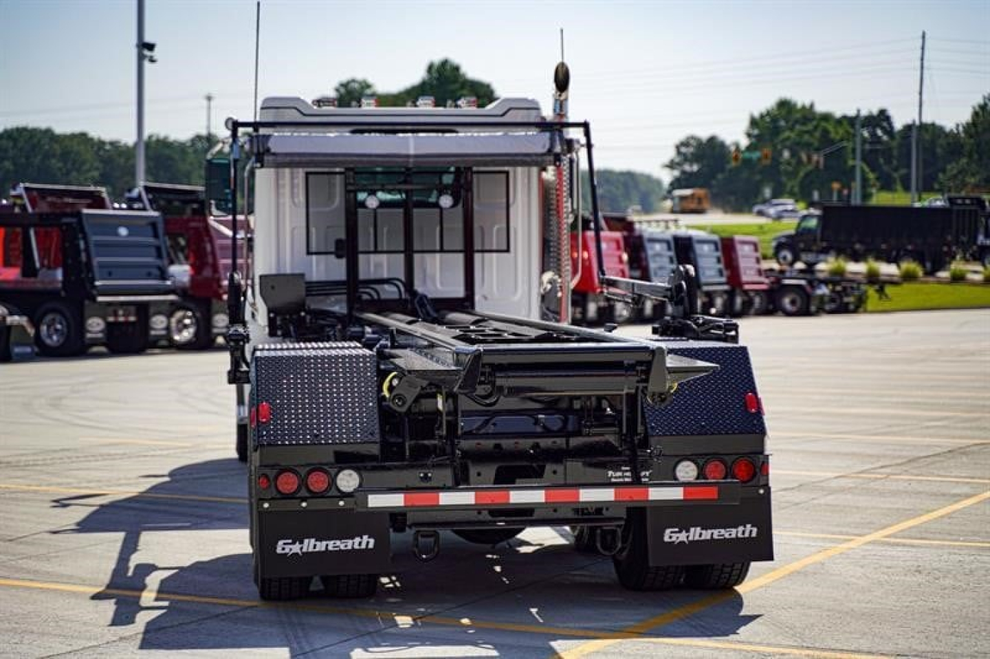 Back view of a new Western Star 47X roll-off truck with loading arm, rear storage boxes, and taillights in a dealership lot.