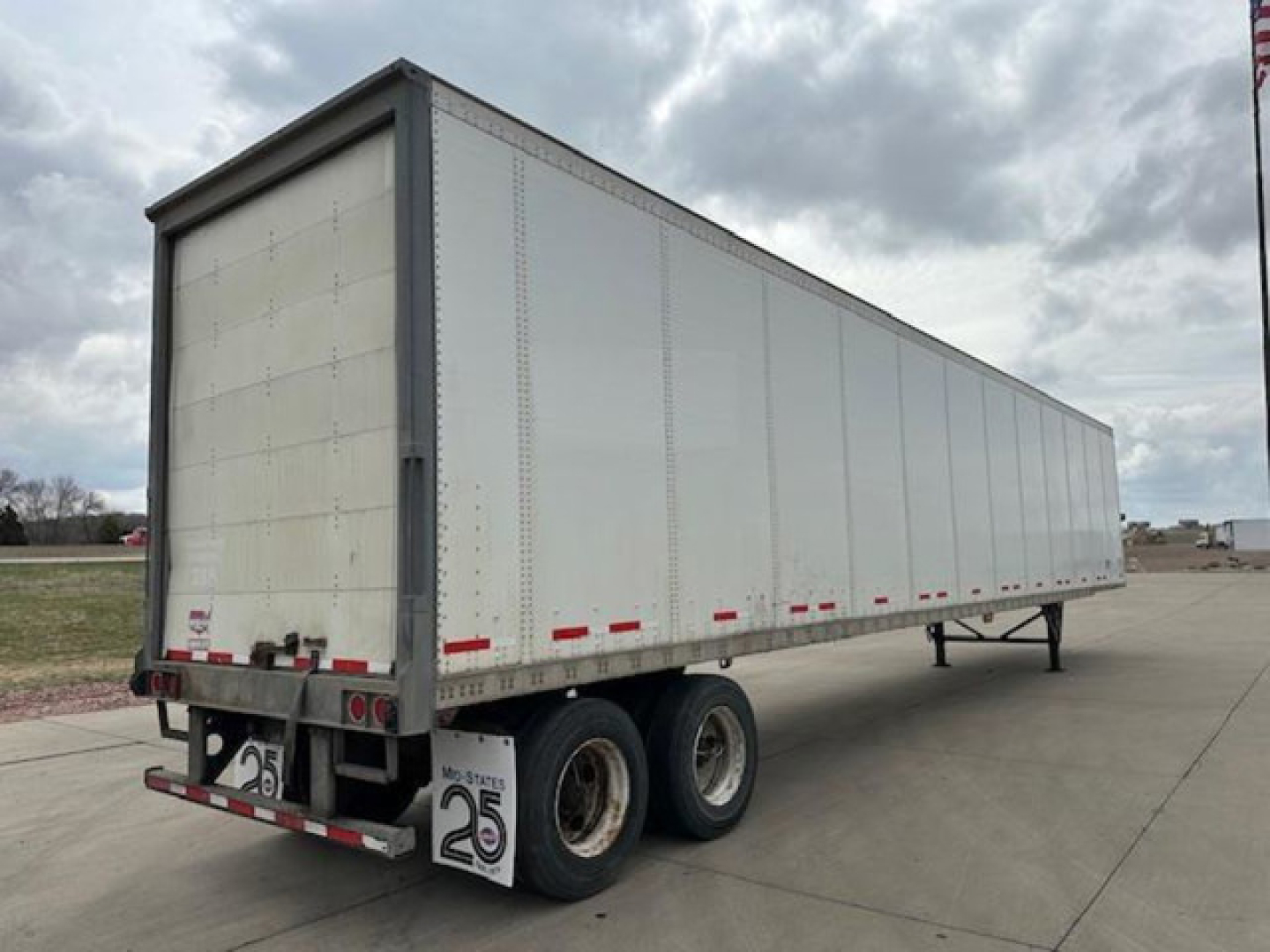 Trailer side view of a 2016 Wabash van trailer with three-axle rear set, silver standard panel sides, rear doors, and reflective safety tape.