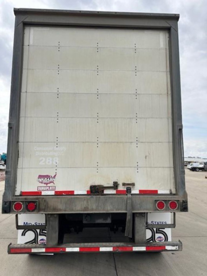 Rear of a Wabash van trailer showing back doors, taillights, and reflective tape. Visible text includes stock area markings and small decals near the bumper.