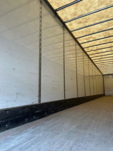 Trailer interior showing empty van cargo area with white walls and ceiling beams.