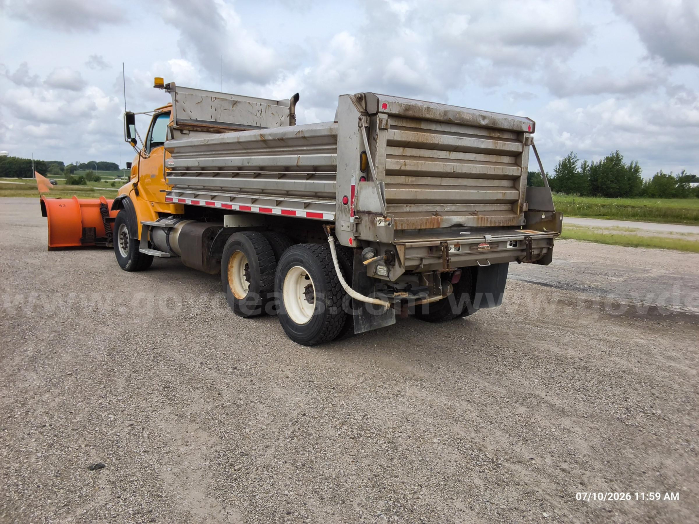 Dump truck with aluminum-sided dump bed showing Sterling LT8500 rear and tires, with a snow plow behind in a gravel lot.