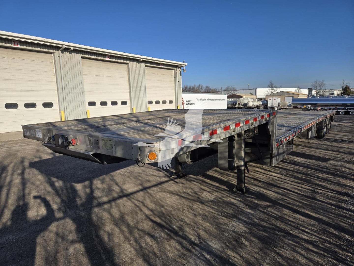 Flatbed trailer in an outdoor lot showing a long aluminum deck with multiple axles and drop deck sections.