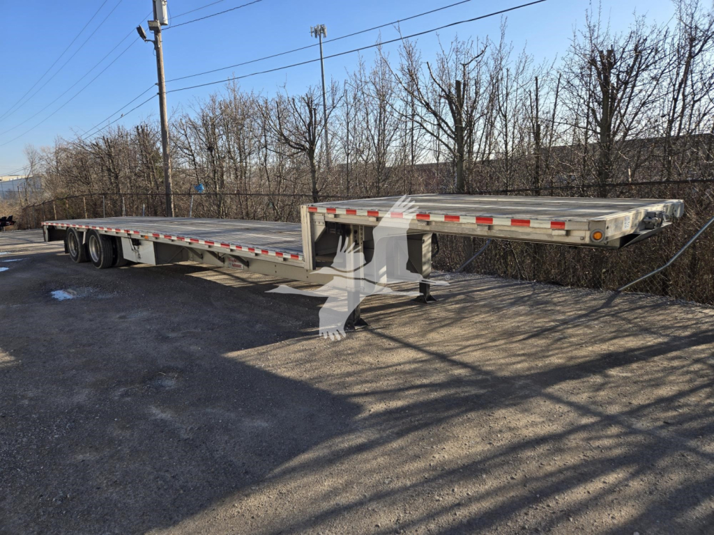 2019 Reitnouer Dropmiser trailer with flatbed deck, gooseneck hitch, dual tandem axles, and reflective safety tape along sides.