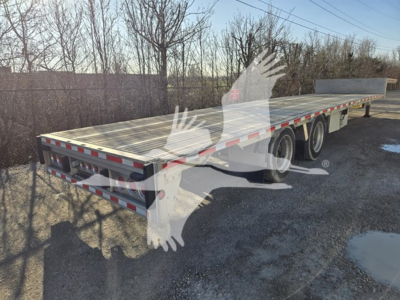 Flatbed trailer showing drop deck with triple-axle configuration and reflective red/white tape along rear edge.