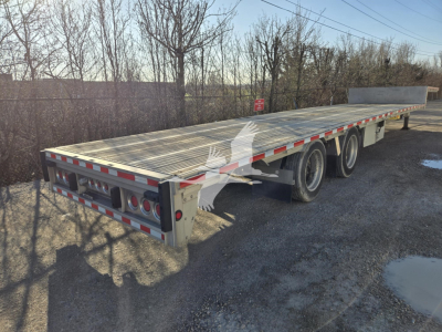 Trailer showing a long aluminum deck with three axles and rear lights; side rails and drop deck mechanism visible.