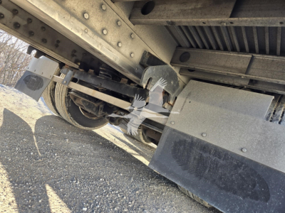 Underneath view of a 2019 Reitnouer Dropmiser trailer showing suspension beams, axles, and a wheel. Visible components include metal girders, bolt connections, and a small portion of the deck edge.