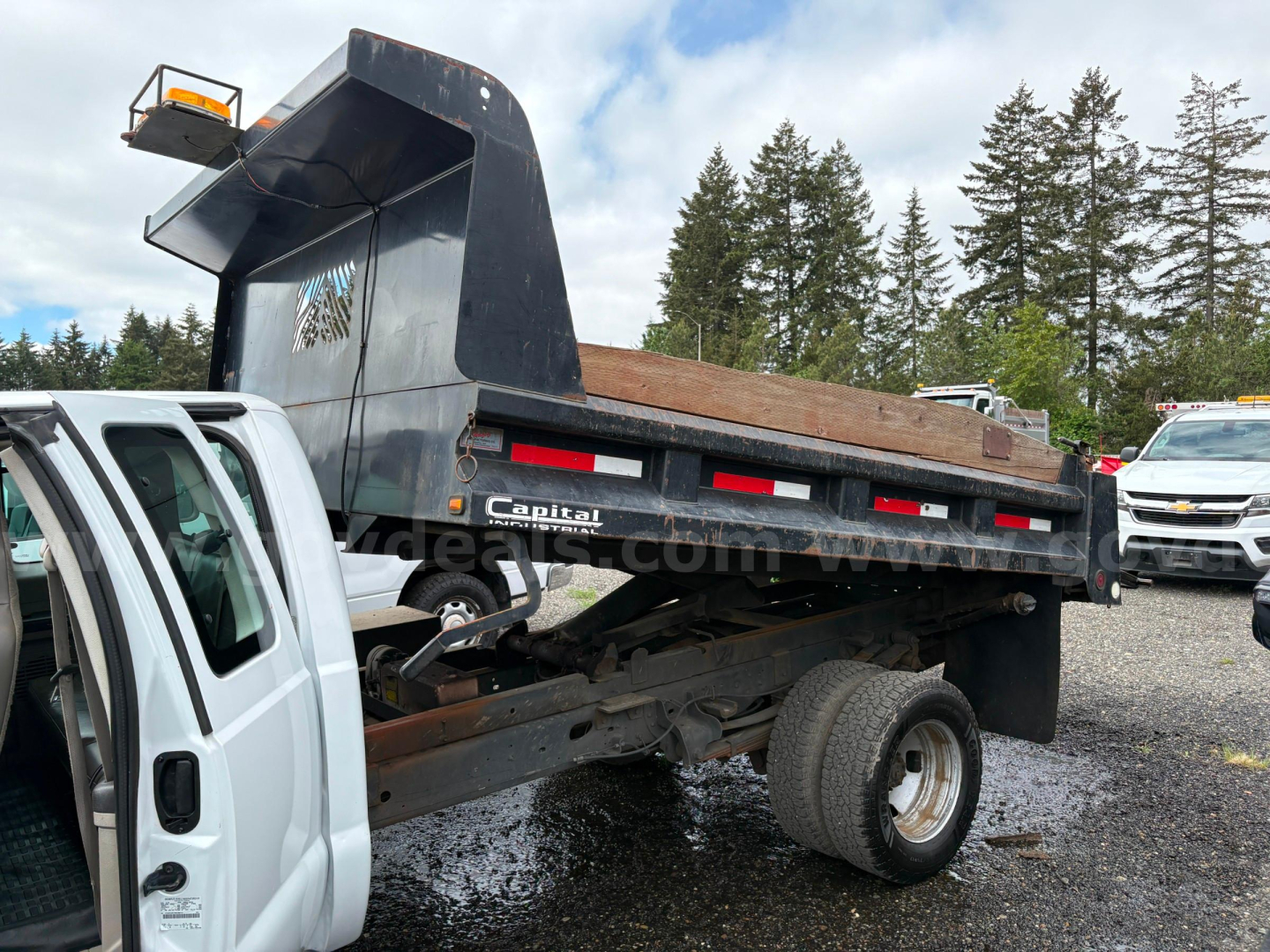 Dump bed truck rear showing dump body and chassis with wheel, side rails, and taillights; Ford F-350 truck bed under elevated dump container.