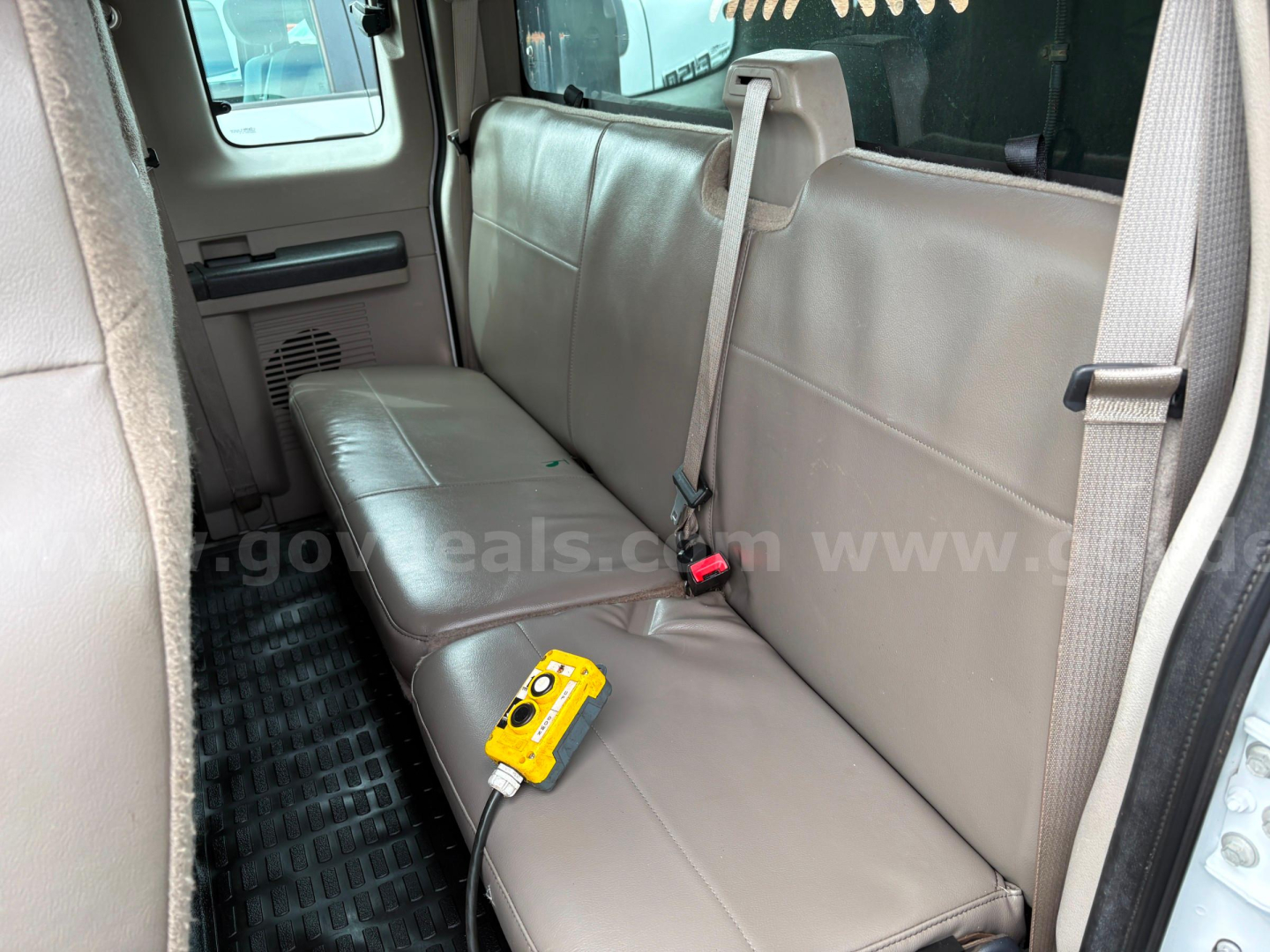 Ford F-350 truck interior rear bench seat with seat belt and a yellow diagnostic tool connected to a cord.