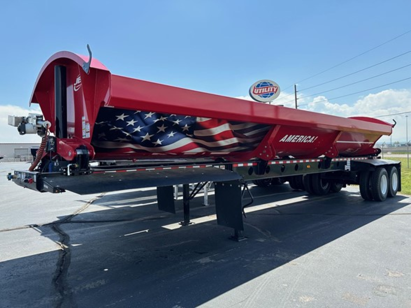 Red Jet Jet side dump trailer with American flag graphic, extended low-clearance tilt, dual rear axles, parked on pavement.