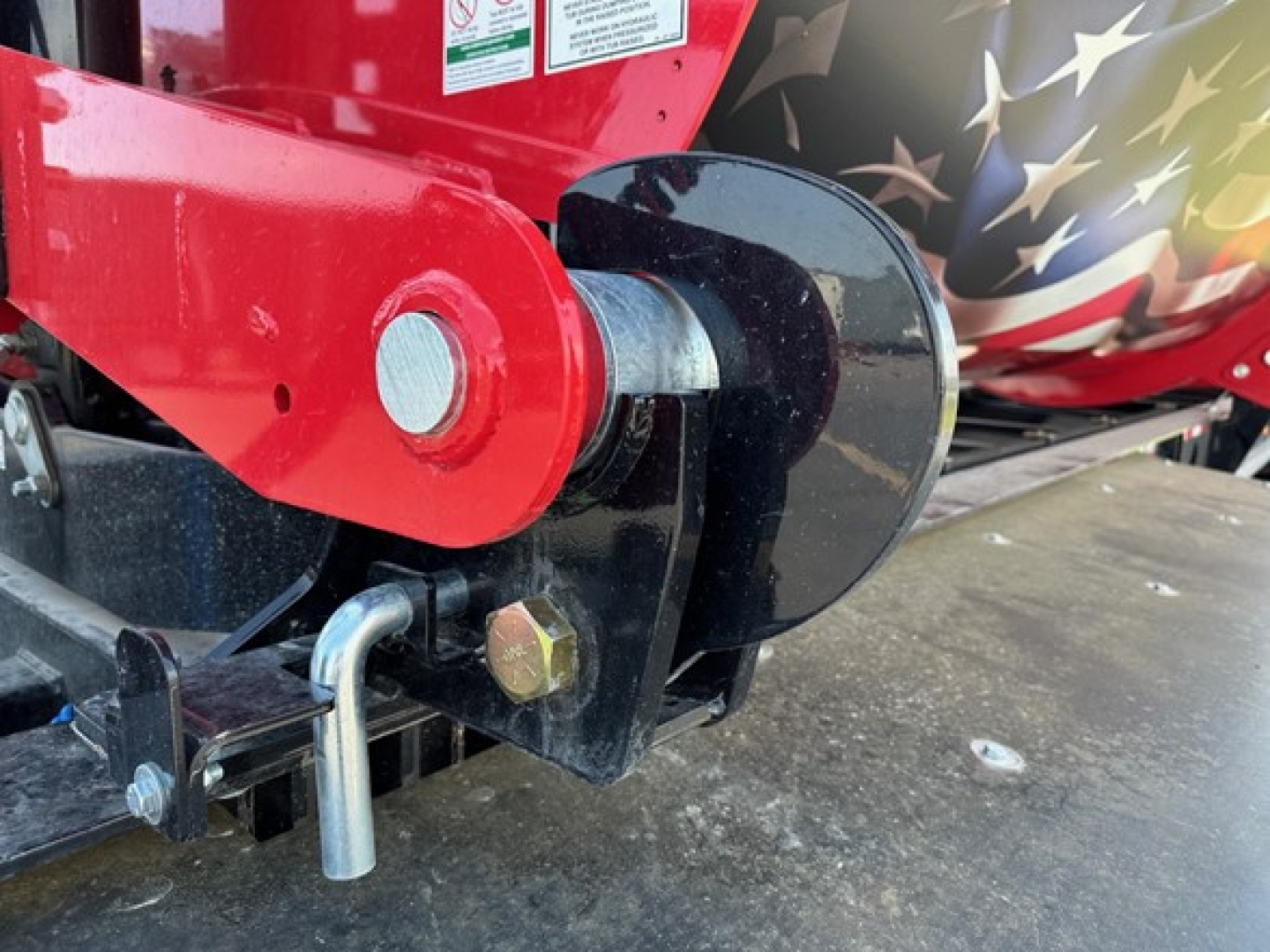 Jet side dump trailer hitch mechanism with red articulating arm and black shackle, visible bolt, pin, and curved hitching jaw.