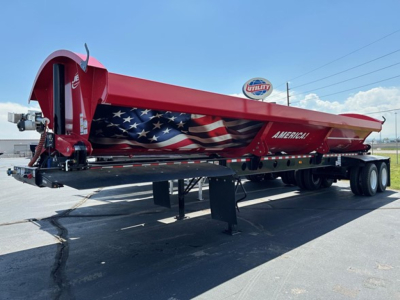 Red Jet Jet side dump trailer with American flag graphic, extended low-clearance tilt, dual rear axles, parked on pavement.