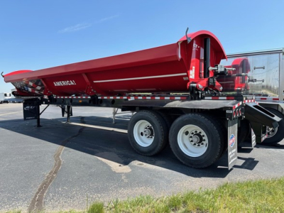 Trailer side dump hopper on a flatbed trailer with red hopper and black chassis showing AMERICAN brand on side, dual rear wheels, and support legs.