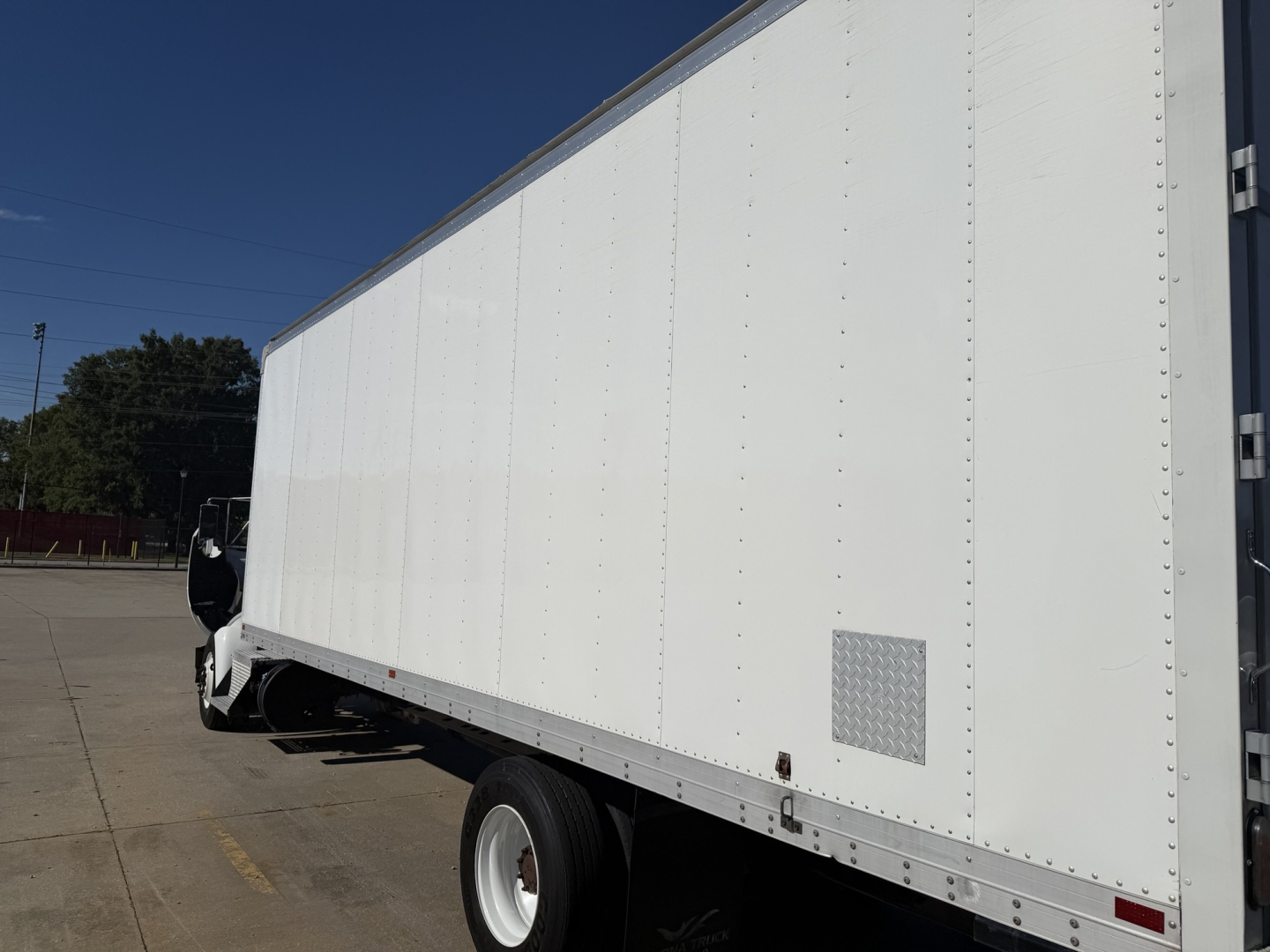Box truck side view showing large white cargo box and front cab of a Kenworth T270, with wheel, reflective trim, and small access panel.