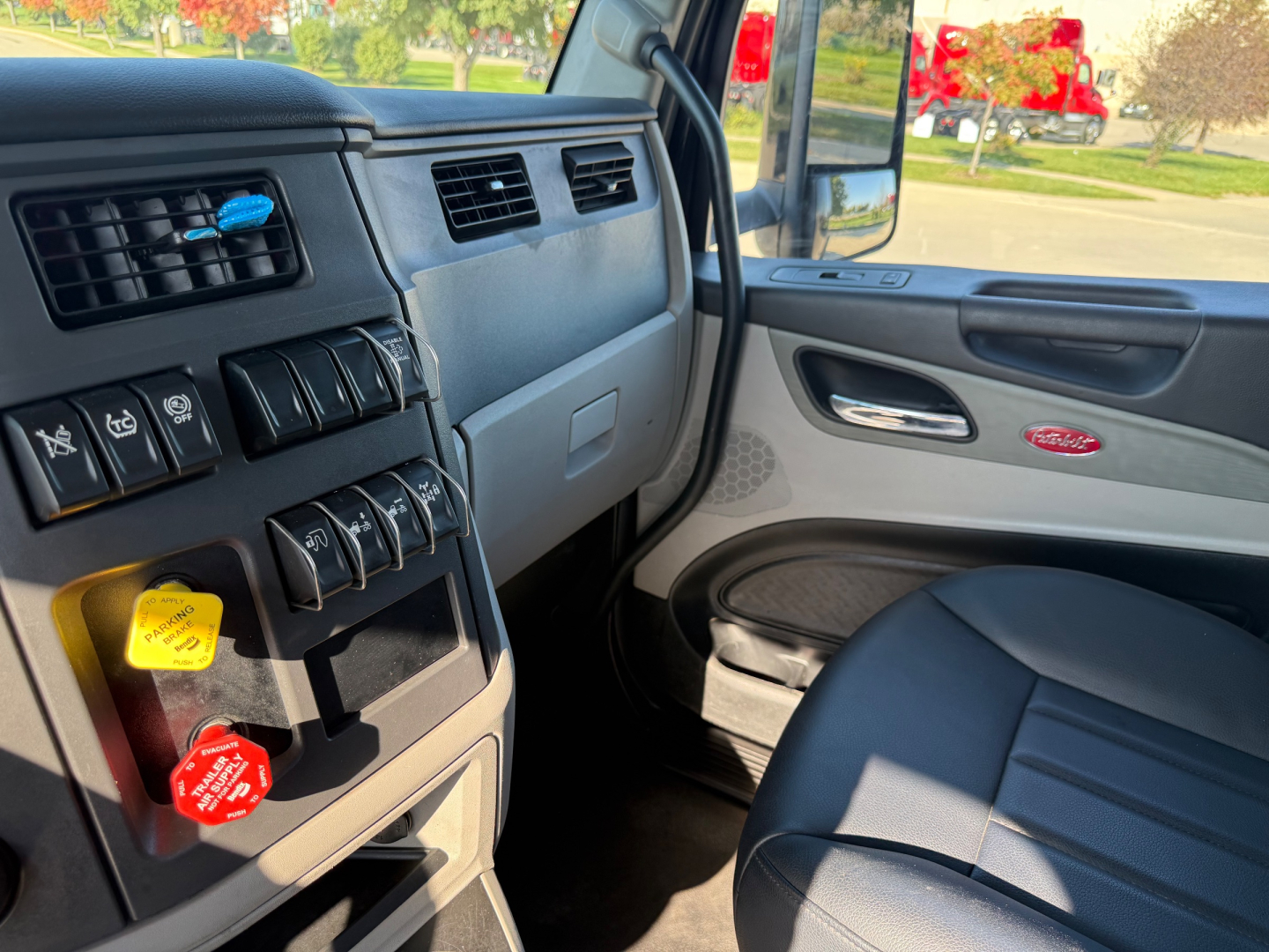 Peterbilt 579 truck cabin interior showing dashboard switches, air vents, ignition area, and passenger door with badge.