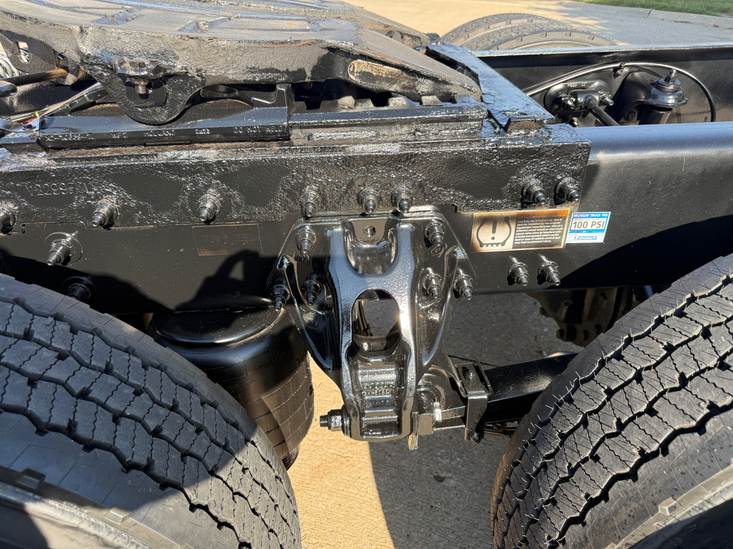Conventional daycab tractor chassis showing front suspension and frame with mounting brackets and a blue sticker, engine bay area not visible.