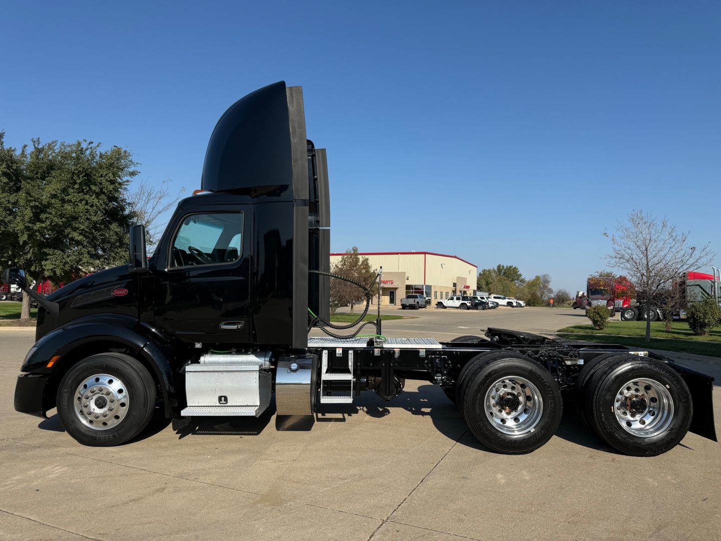 Peterbilt 579 conventional daycab tractor in black, side view showing tall sleeper/hood, polished steel fuel tanks, chrome wheels, and three rear axles.