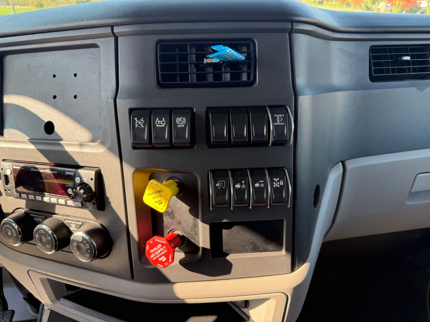 Peterbilt 579 dash area showing control switches and red/black knobs; dashboard vents and center stack; yellow and red engine start/stop knobs; climate controls; radio and instrument panel edges visible.